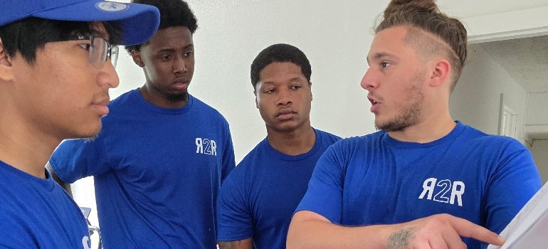 Residential Movers 3 A group of four individuals in matching blue t-shirts, engaged in conversation and collaboration in a bright, minimalistic space.