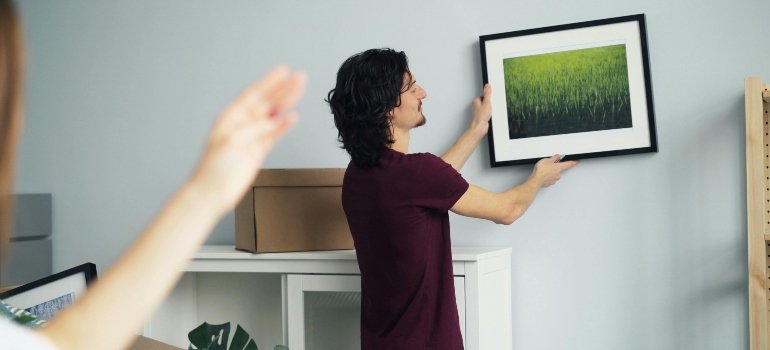 Practical checklist of things you need when moving out 2 Man hanging a framed picture after unpacking in a new living room