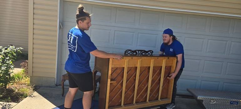 two Goshen Movers carrying a heavy piece of furniture 