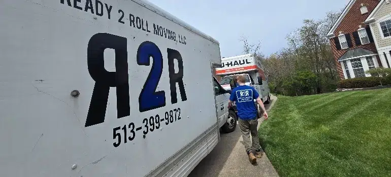 A moving truck with the logo "R2R" and a worker in a blue shirt walking towards a U-Haul truck in a residential area.