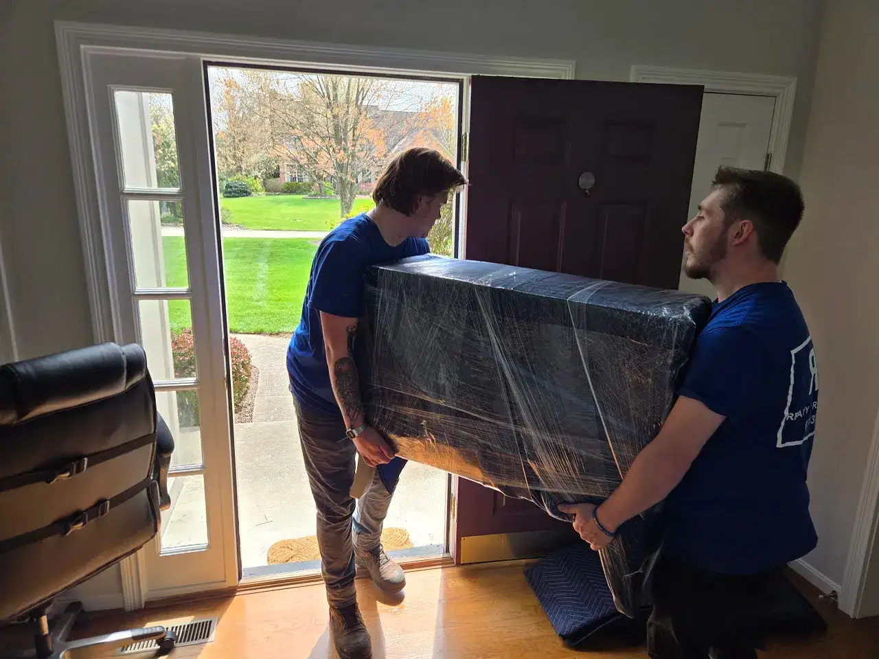 Professional movers carrying wrapped furniture through front doorway