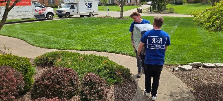 Furniture Movers 4 Two men carrying a large box together on a sidewalk, demonstrating teamwork and effort in their task.