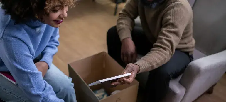 Preparing for movers: What to do the week before your move 3 A couple smiling while sorting items from a moving box, sharing a moment during Preparing for Movers.
