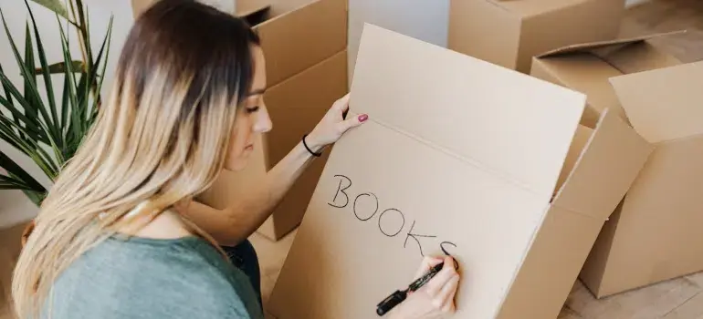 The best way to pack books for moving 3 Person labeling a sealed moving box as books