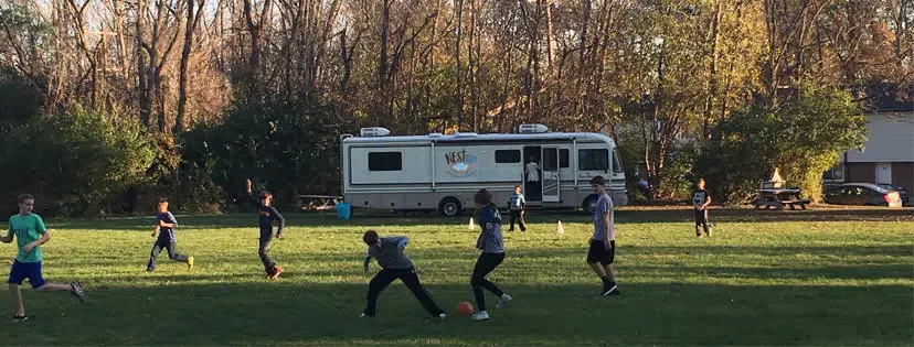 Kids playing on the grass in front of the Nest bus