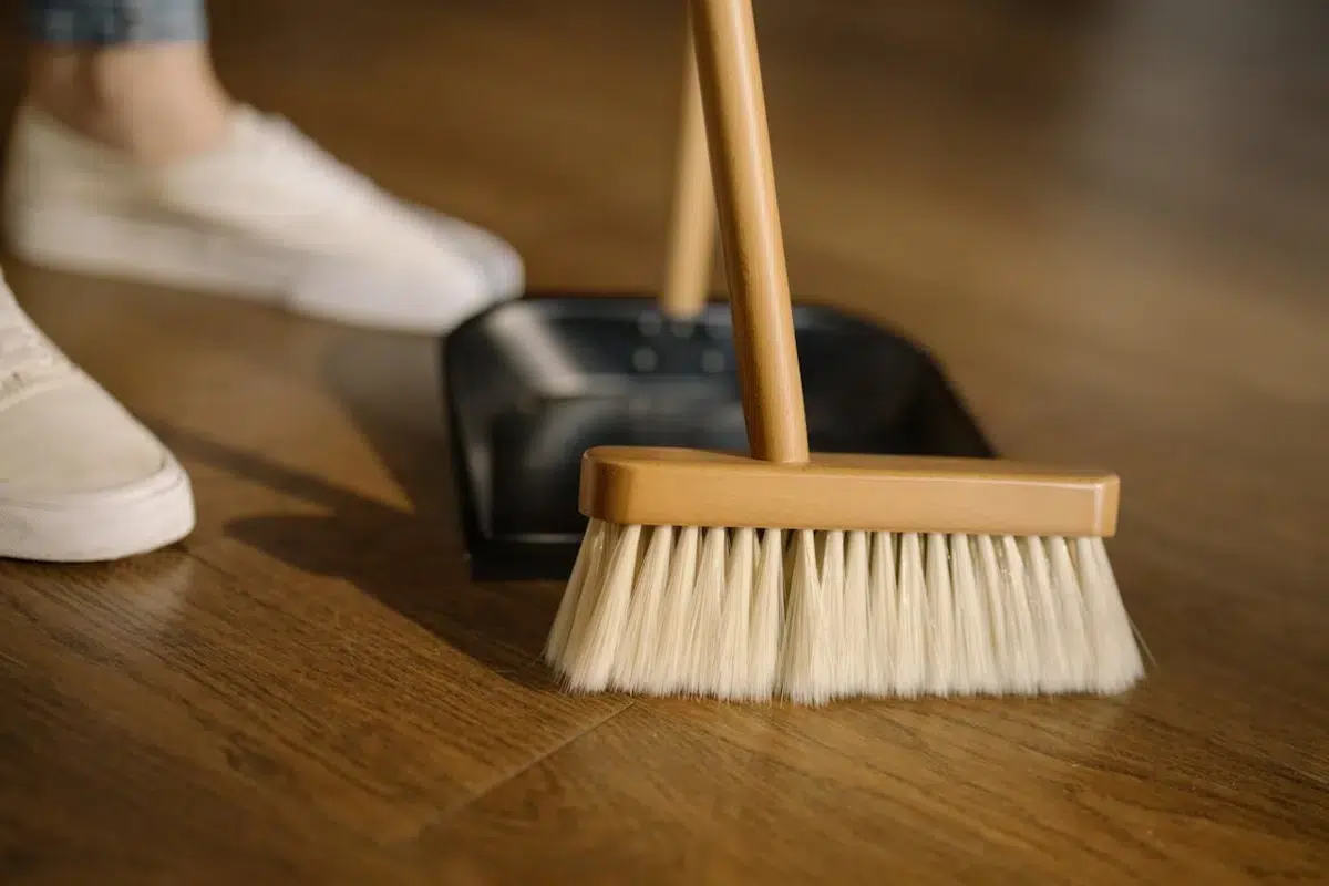 How to clean an apartment before moving in, shown with a wooden broom and dustpan on a polished wooden floor