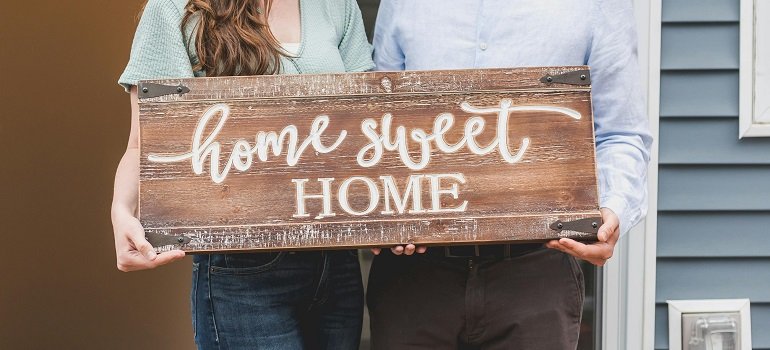 Avoid move-in day problems by checking HOA apartment and subdivision rules in Ohio 3 a couple who follows HOA apartment and subdivision rules in Ohio holding a welcome sign